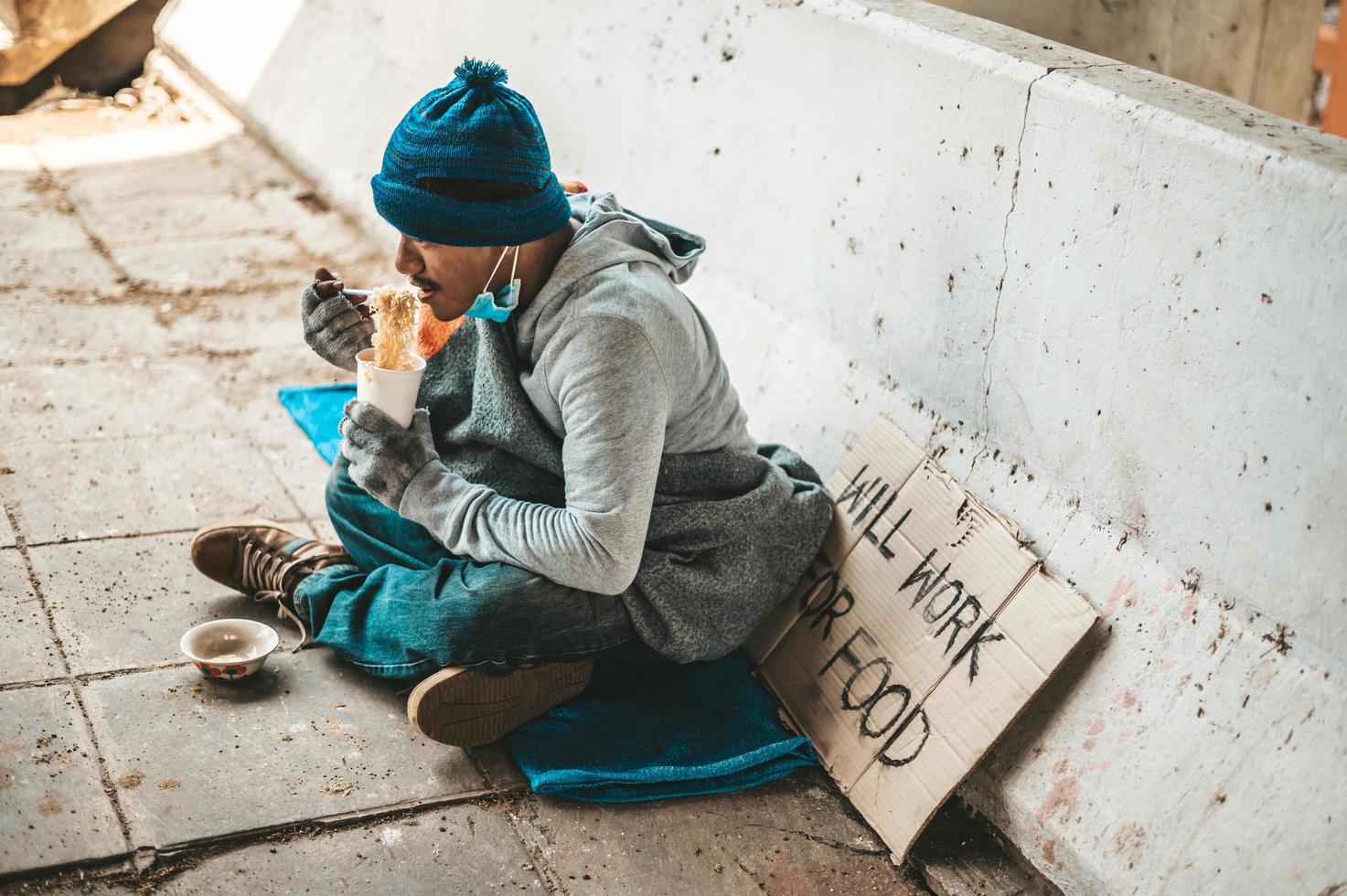 senzatetto avvolto in un panno e mangiare spaghetti foto