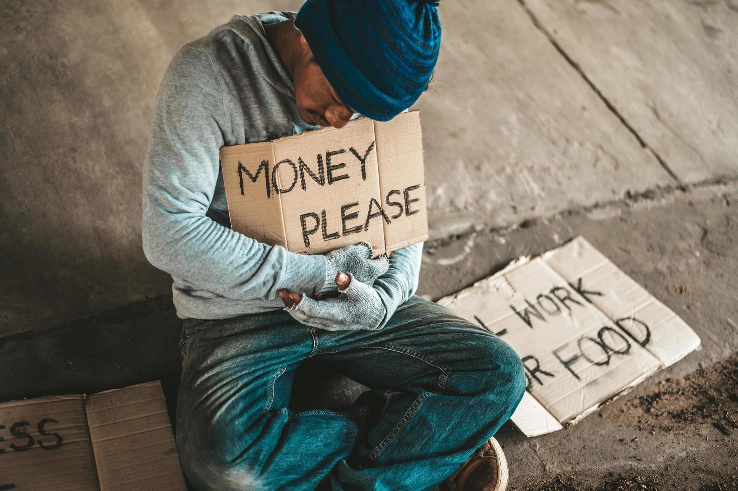 mendicante seduto sotto un ponte con un segno, soldi per favore foto