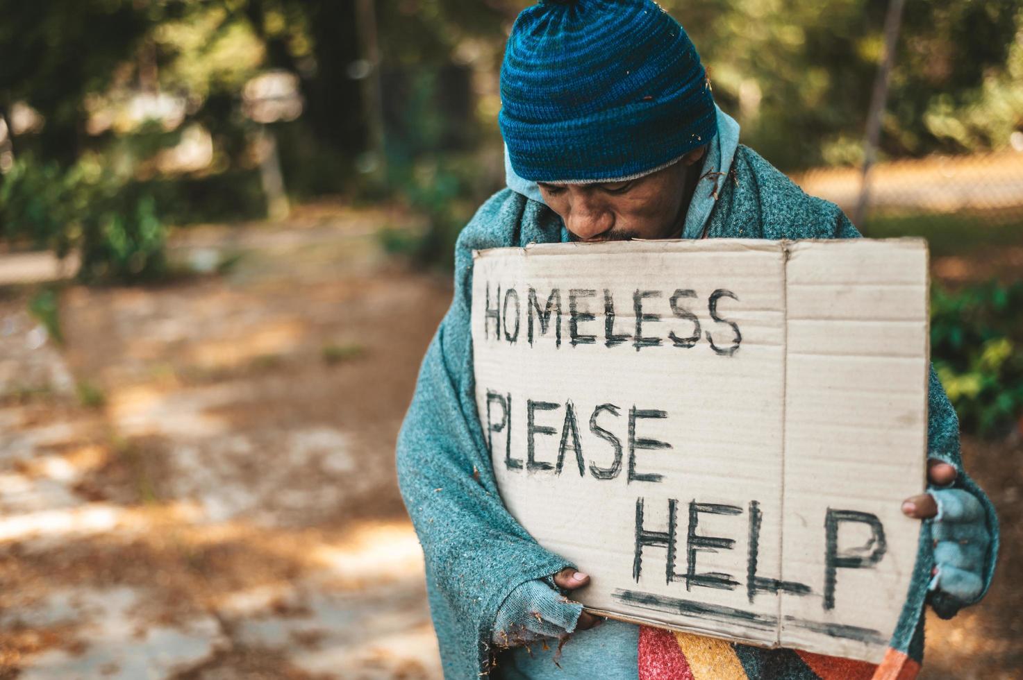 mendicante sta sulla strada con per favore aiuto segno foto