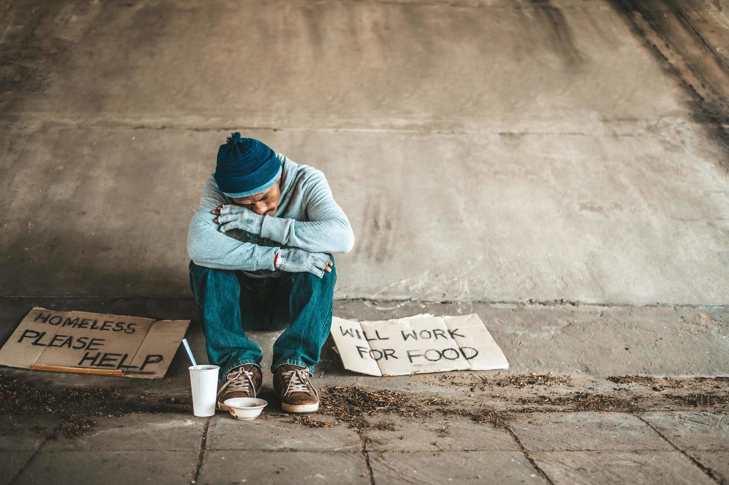 mendicanti seduti sotto il ponte con cartelli di aiuto foto