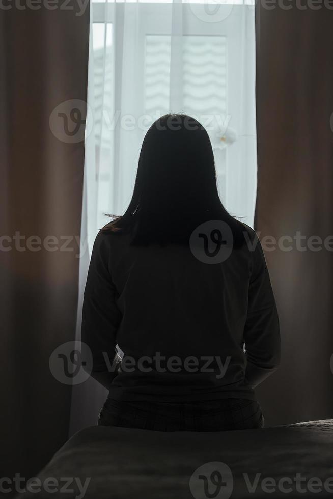 silhouette di un' giovane donna nel pigiama contro il sfondo di un' finestra a casa su un' letto con di stagione affettivo disturbo o depressione.. il concetto di inverno depressione dovuto per mancanza di luce del sole foto