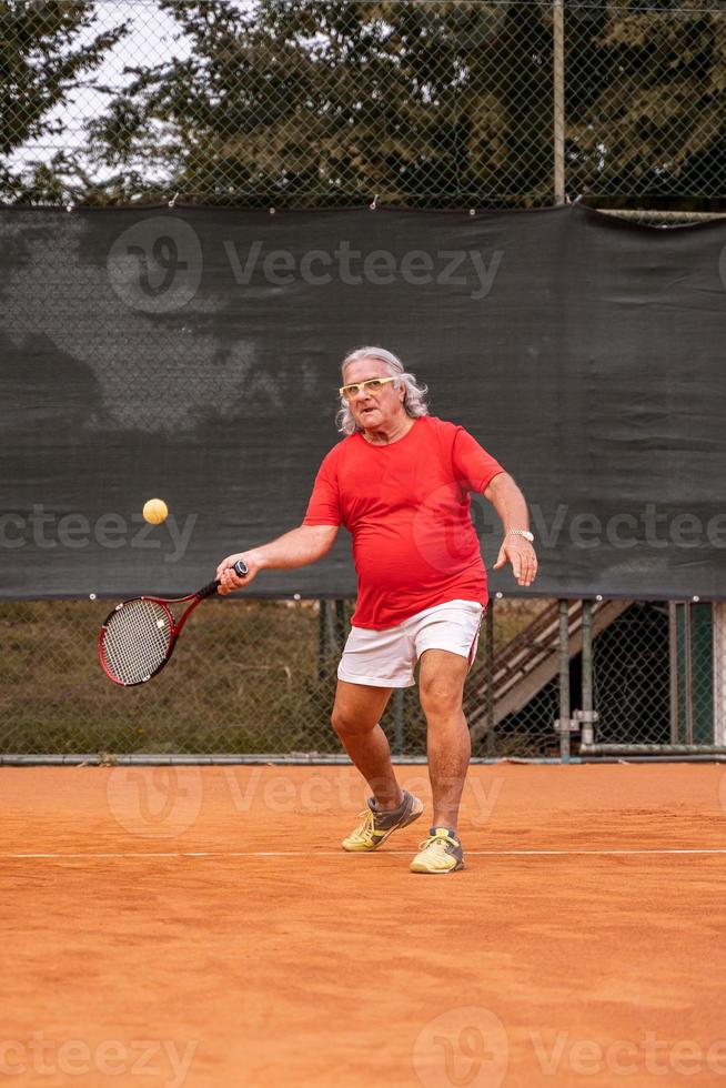 anziano tennis giocatore vestito nel abbigliamento sportivo nel azione su un' argilla tennis Tribunale foto