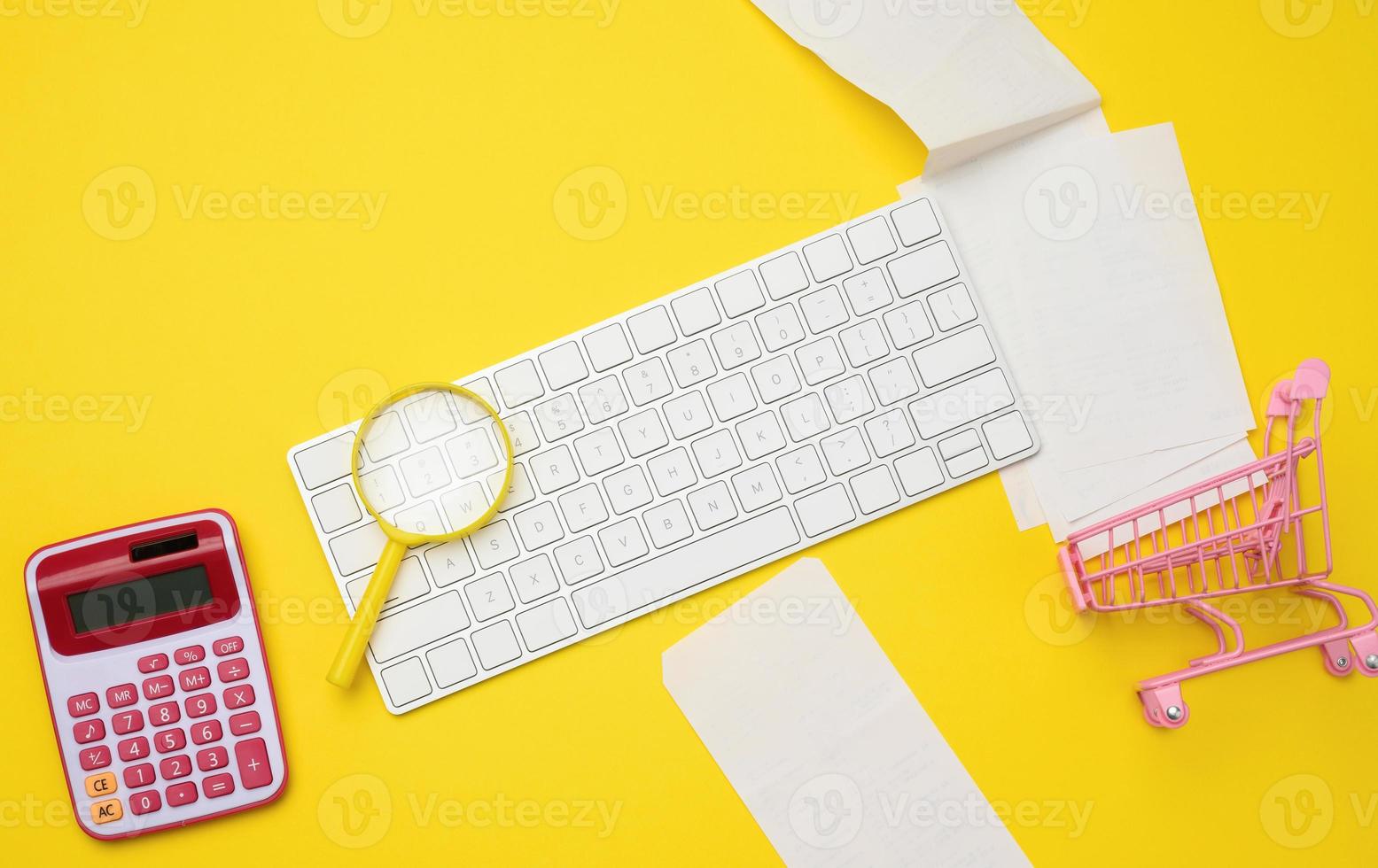 bianca senza fili tastiera del computer, pila di carta ricevute e lente d'ingrandimento su giallo sfondo, bilancio analisi concetto foto
