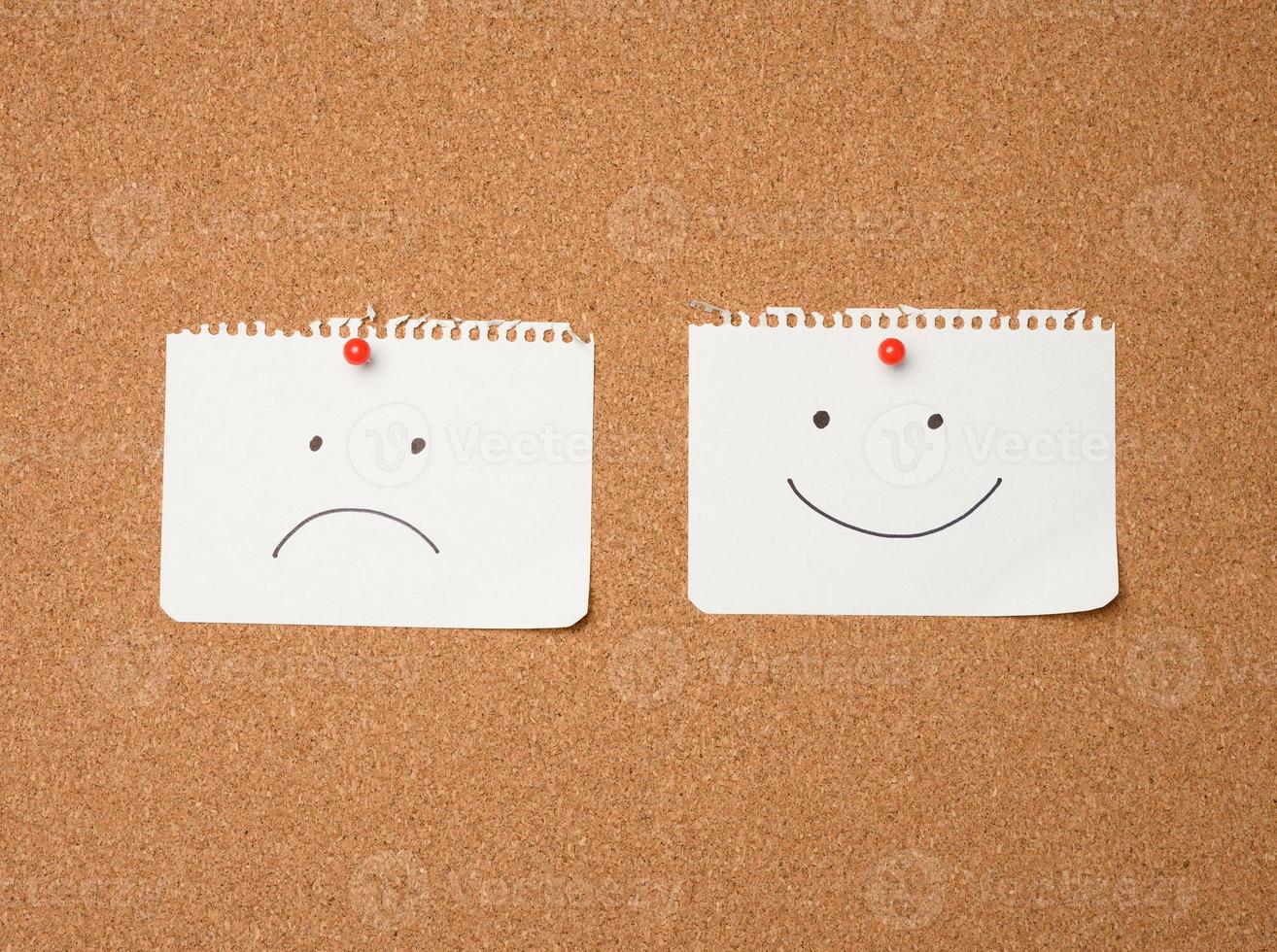 Due carta le foglie con un' Sorridi e un' triste emozione allegato con un' pulsante su un' Marrone tavola foto