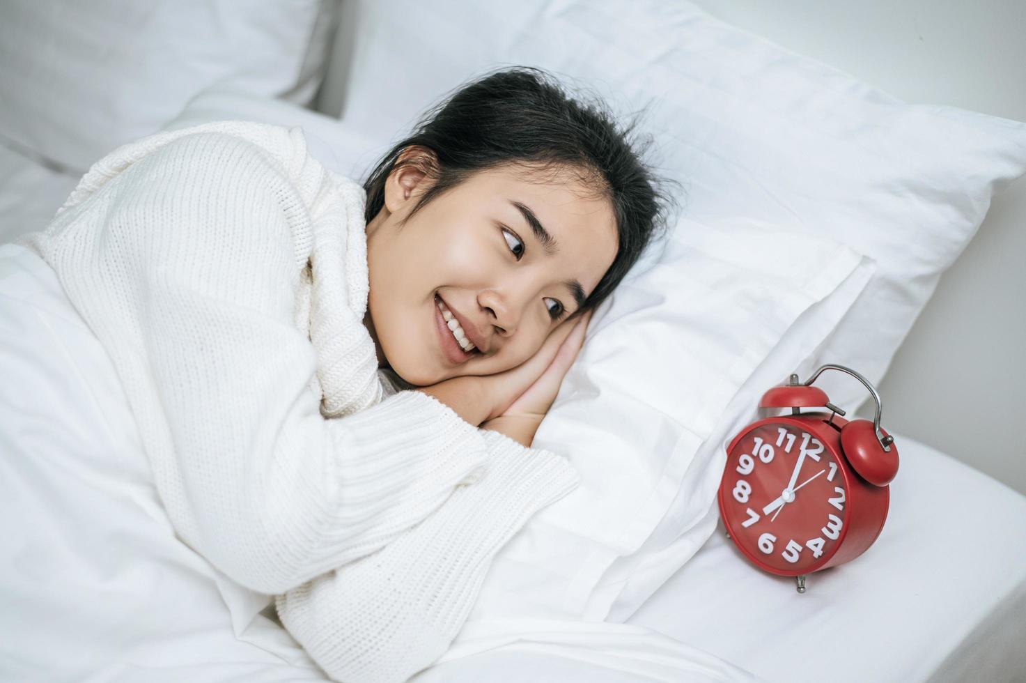 una donna che indossa una camicia bianca sdraiata sul suo letto con una sveglia foto