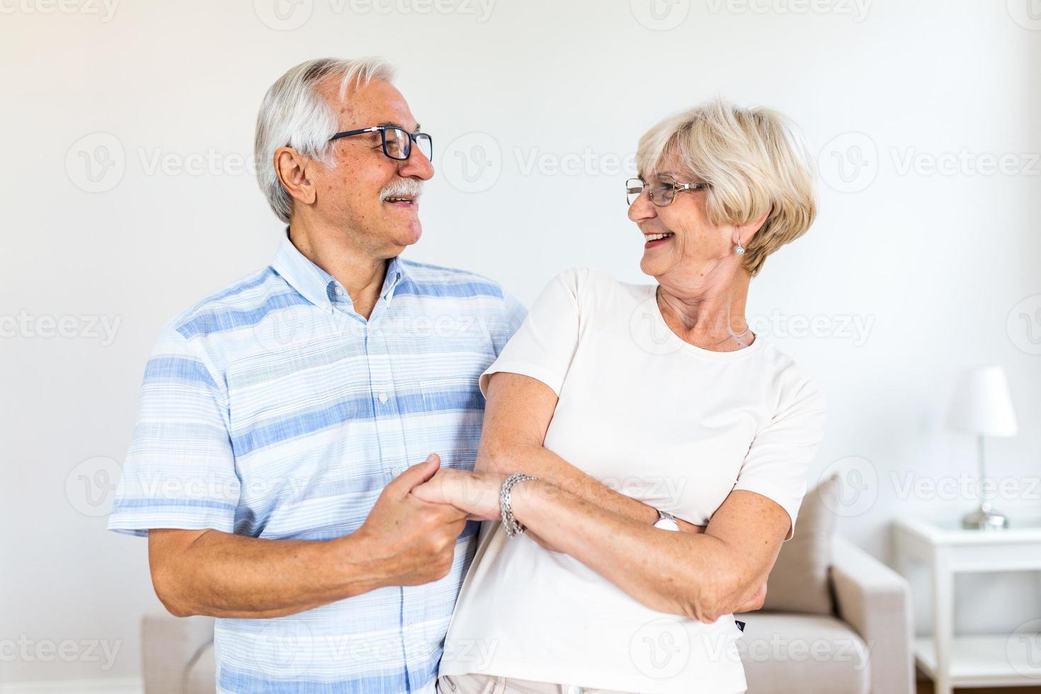 gioioso attivo vecchio pensionato romantico coppia danza ridendo nel vivente camera, contento mezzo anziano moglie e Sambuco marito avendo divertimento a casa, sorridente anziano famiglia nonni rilassante bonding insieme foto