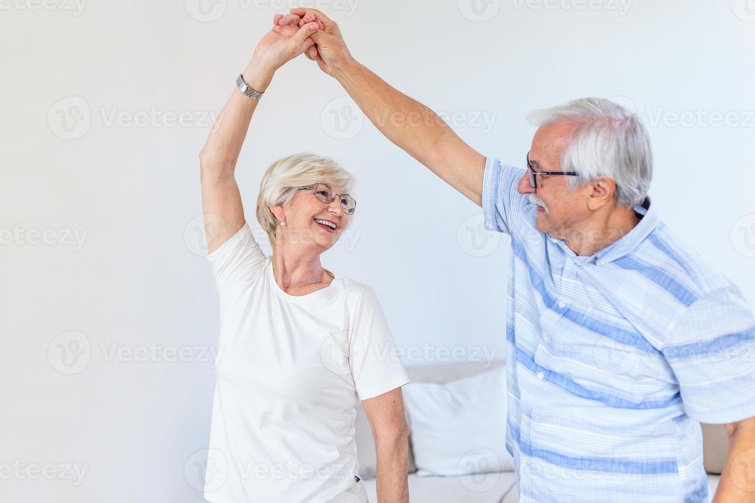 gioioso attivo vecchio pensionato romantico coppia danza ridendo nel vivente camera, contento mezzo anziano moglie e Sambuco marito avendo divertimento a casa, sorridente anziano famiglia nonni rilassante bonding insieme foto