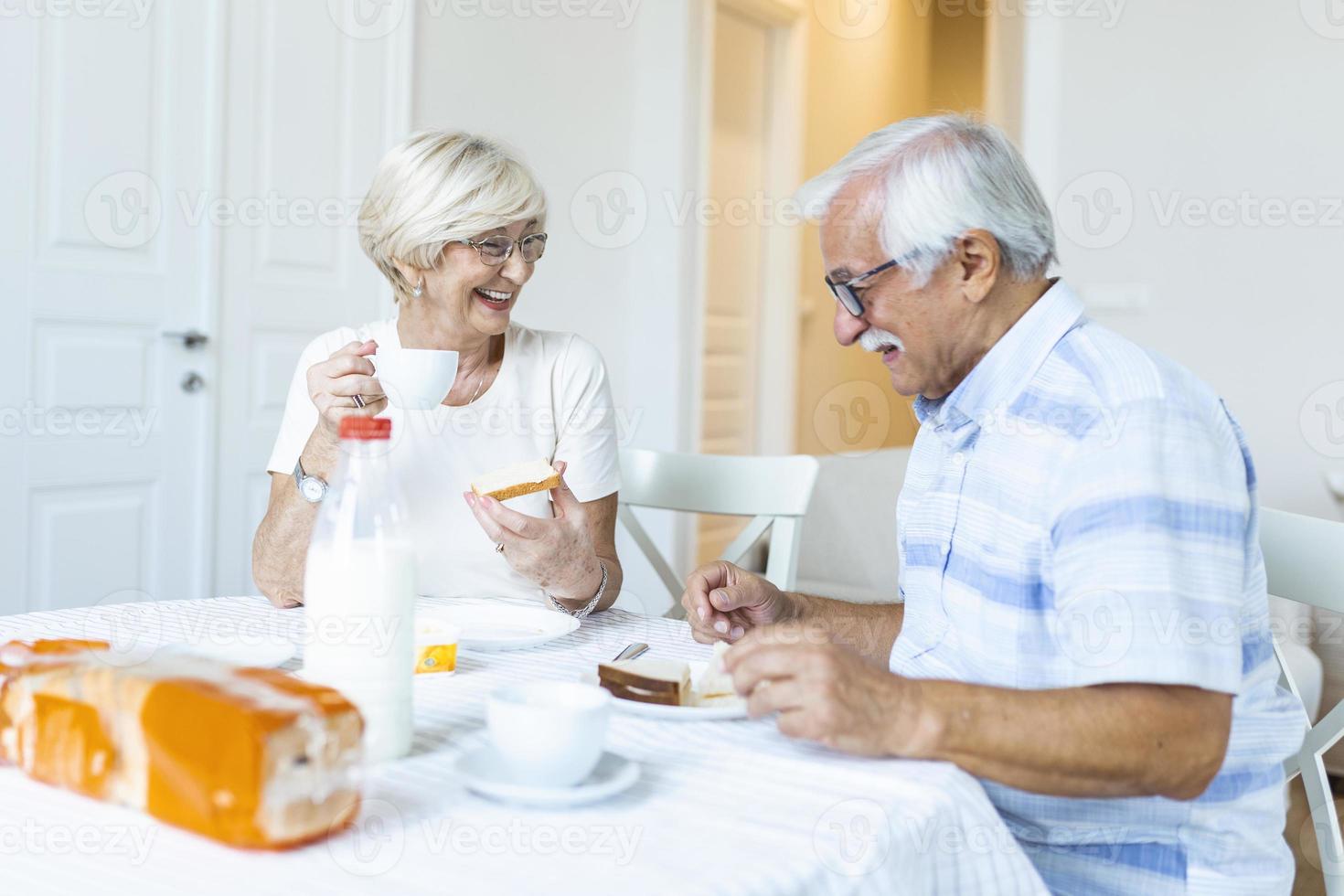 contento anziano coppia avendo prima colazione a casa. anziano coppia sorridente per ogni Altro. vecchio coppia avendo divertimento durante prima colazione. cibo, mangiare, persone e salutare cibo concetto foto