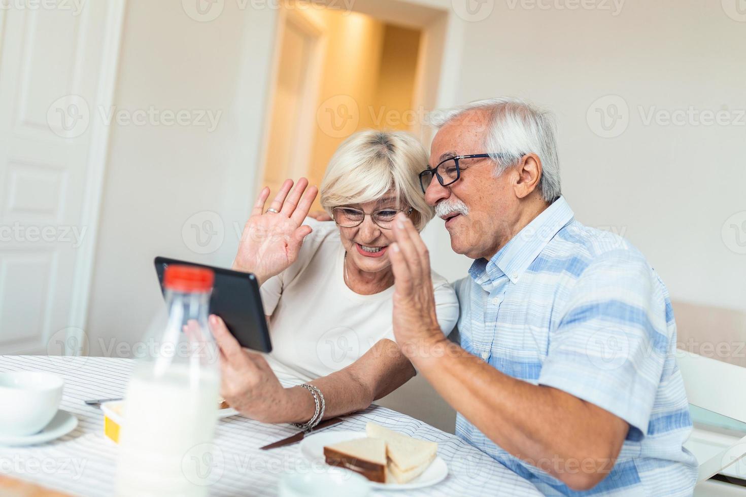 anziano uomo e il suo moglie siamo utilizzando un' digitale tavoletta e comunicare con loro bambini. contento anziano coppia è avendo prima colazione e avendo un in linea conversazione con loro famiglia e invio saluti. foto