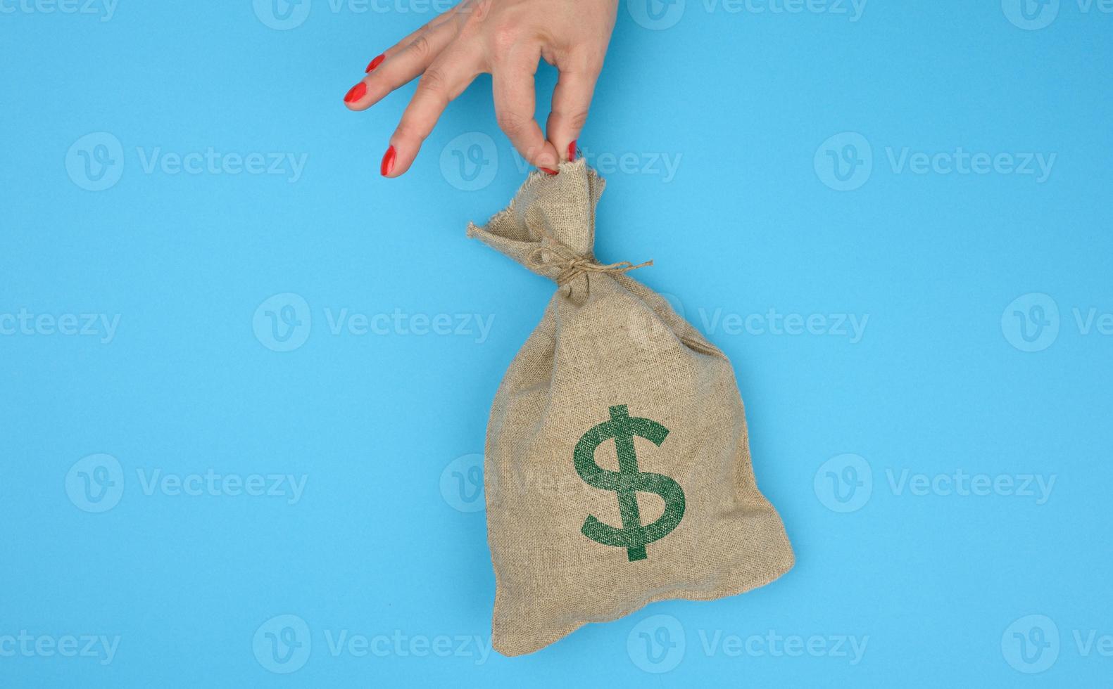 mano detiene un' tela Borsa pieno di i soldi con un' noi dollaro icona su un' blu sfondo foto