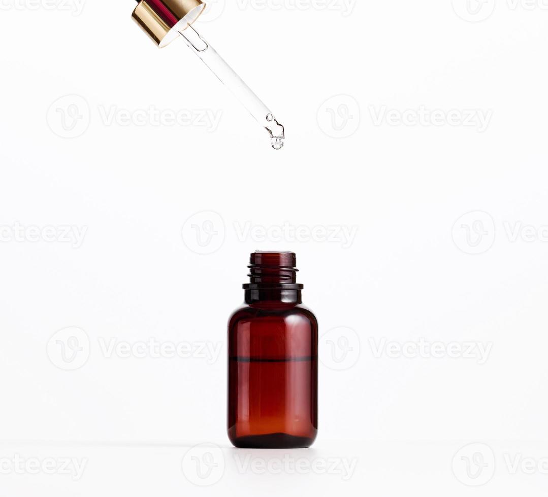 essenziale olio caduta a partire dal il ambra bicchiere contagocce. blu bottiglia di cosmetico olio con un' pipetta, bianca sfondo foto