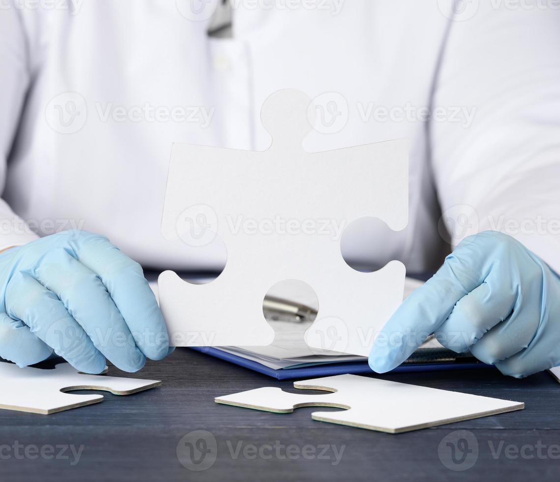 il medico si siede a il tavolo e detiene un' carta bianca puzzle. soluzione concetto foto