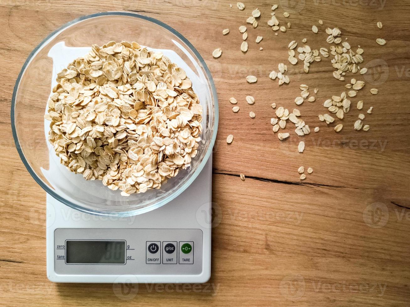 fiocchi d'avena pesatura nel bicchiere ciotola su il cucina bilancia su di legno tavolo. foto