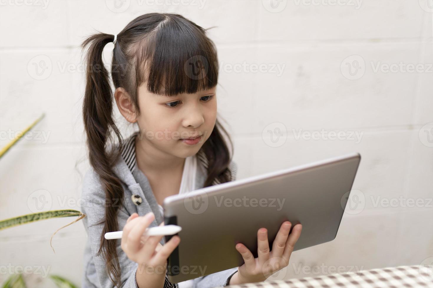 asiatico ragazza con digitale tavoletta e penna studiando in linea a casa. formazione scolastica e distanza apprendimento per bambini. homeschooling durante quarantena. restare a casa intrattenimento. foto