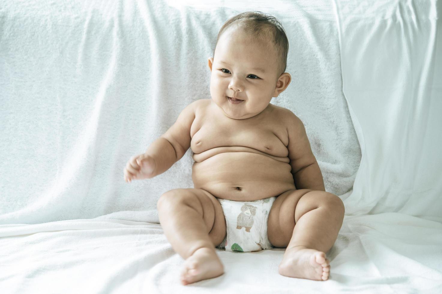 un bambino che impara a sedersi su un letto bianco foto