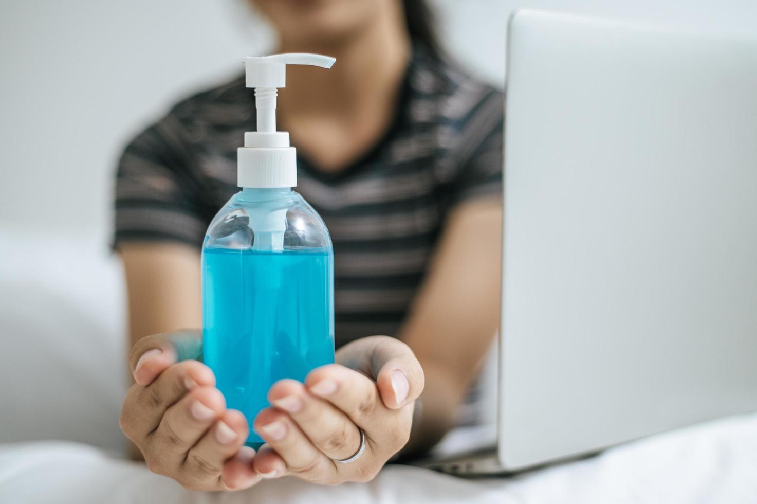 giovane donna sul letto tenendo il gel per il lavaggio delle mani foto