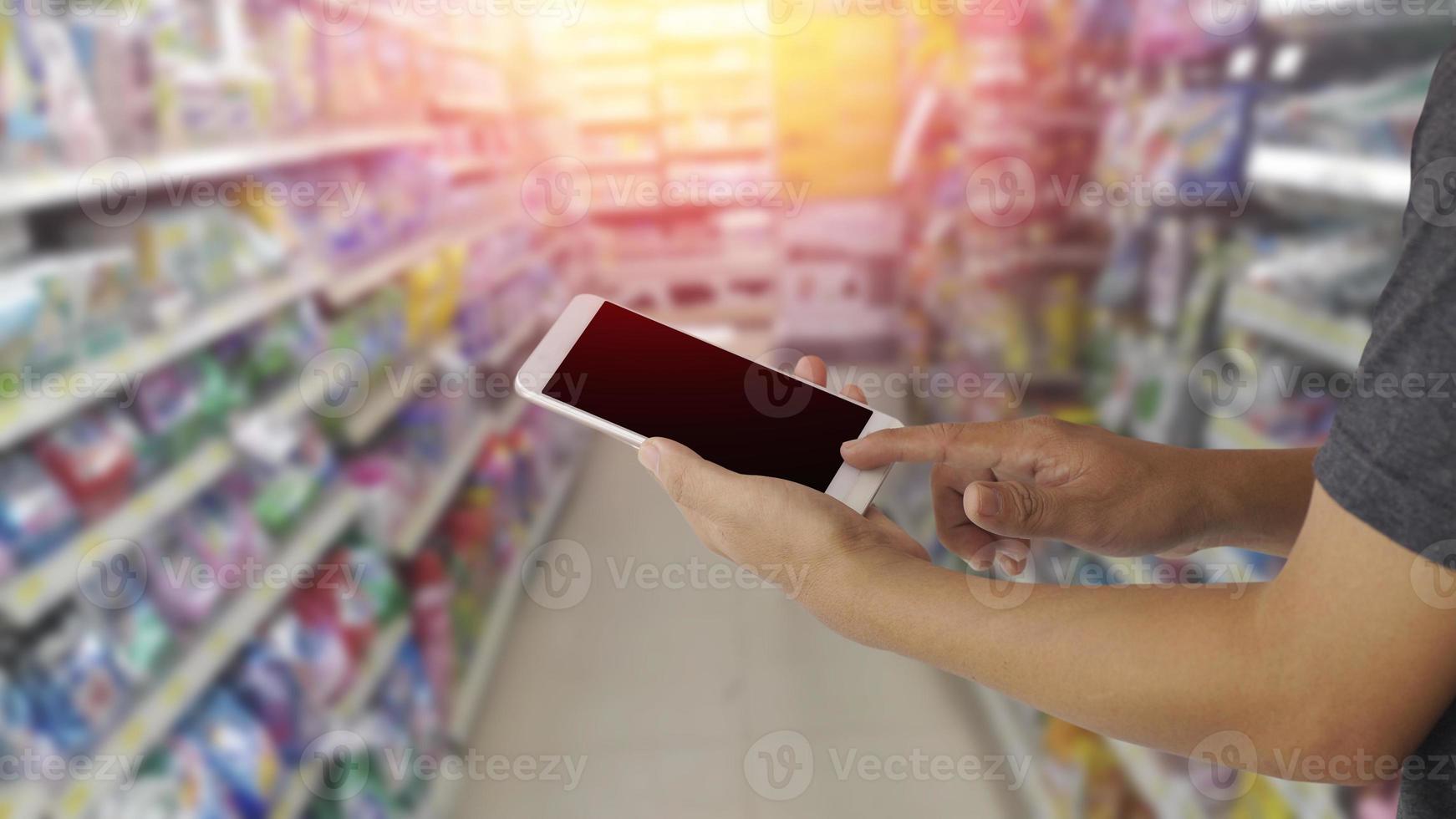 mani utilizzando lo schermo in bianco mobile smart phone con sfondo sfocato nel grande magazzino foto