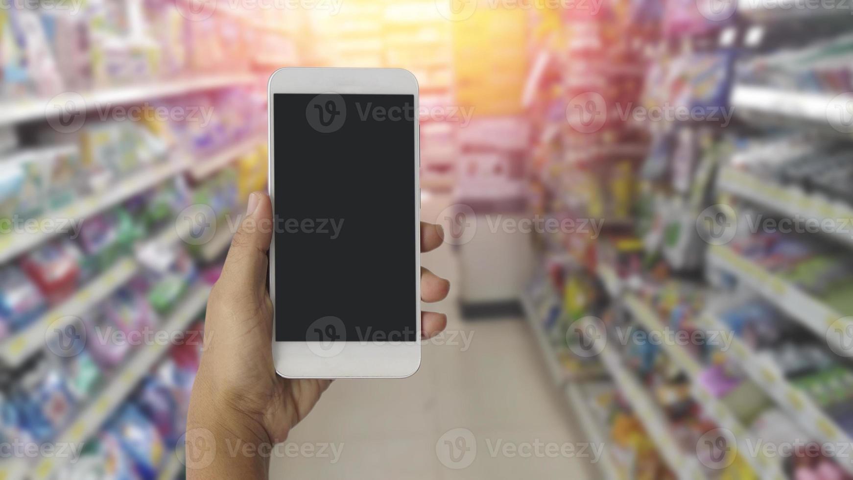 mani utilizzando lo schermo in bianco mobile smart phone con sfondo sfocato nel grande magazzino foto