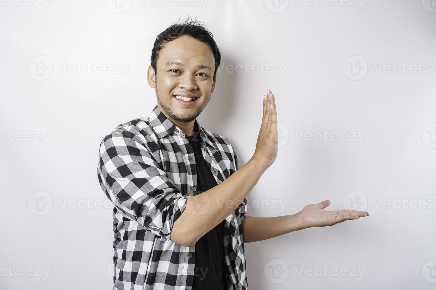 eccitato asiatico uomo indossare tartan camicia è puntamento a il copia spazio accanto lui, isolato di bianca sfondo foto