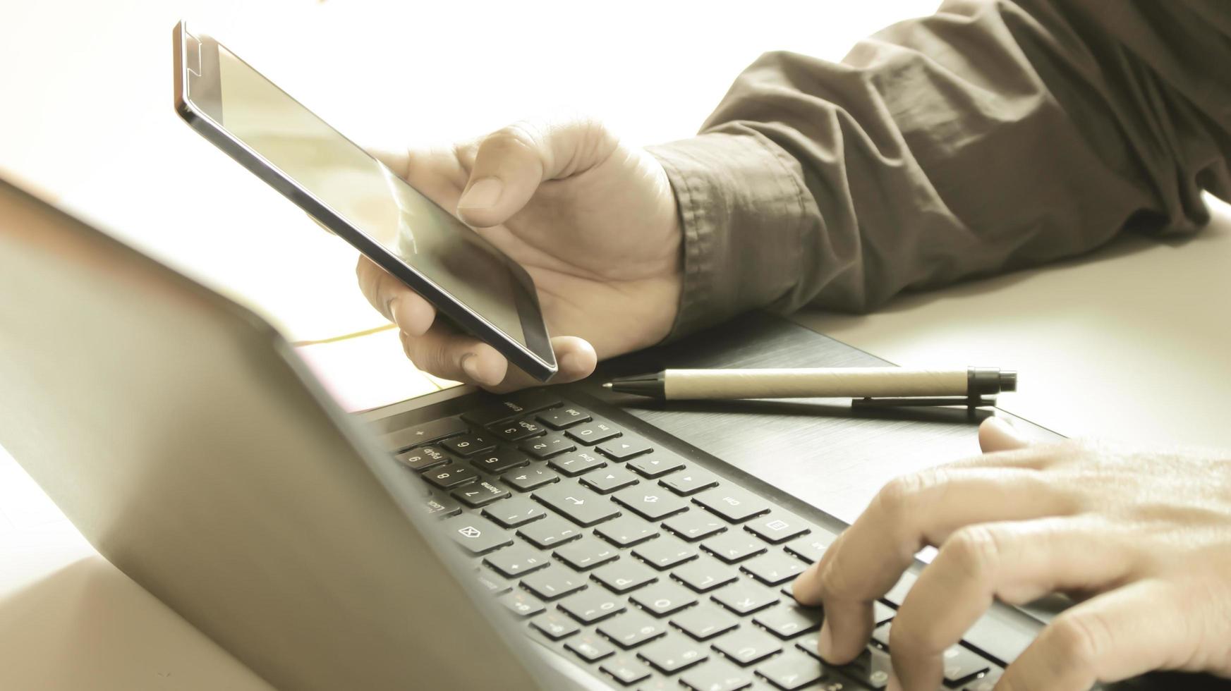 tenendo il telefono professionale e digitando sul computer foto