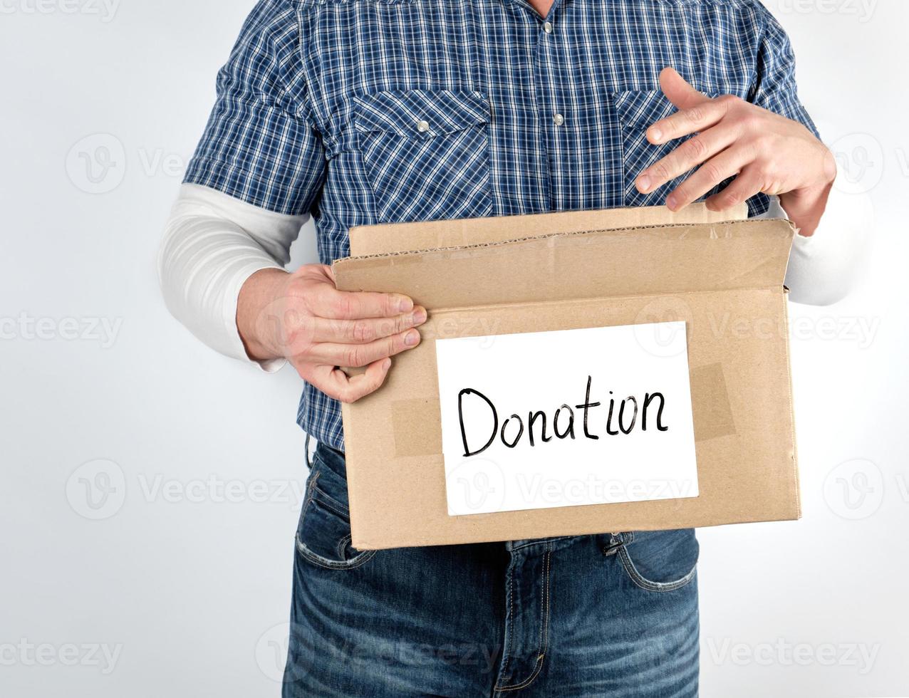 uomo nel un' blu scacchi camicia e jeans detiene un' grande Marrone carta scatola con il iscrizione donazione foto