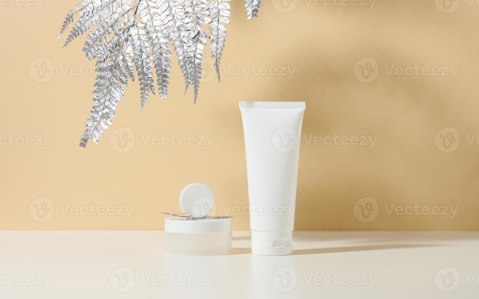 bianca tubo per cosmetici, un' vaso di crema e argento foglia su un' bianca tavolo. cosmetico su un' beige ombra backgroun foto