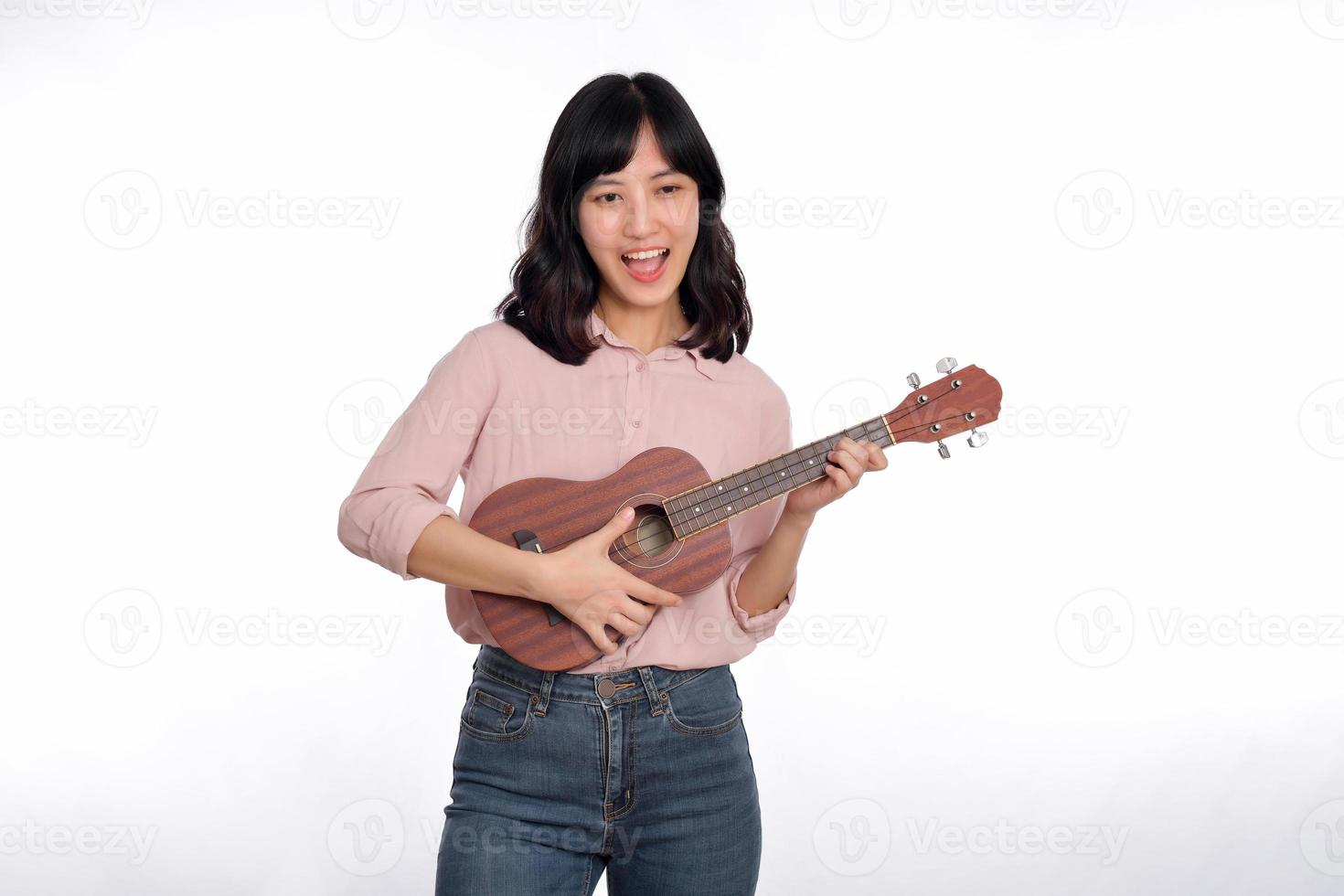 contento giovane asiatico donna con casuale capi di abbigliamento giocando ukulele isolato su bianca sfondo foto