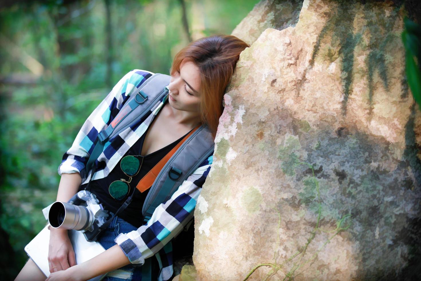 donna viaggiatore provato e appoggiato su una grande roccia in una foresta foto