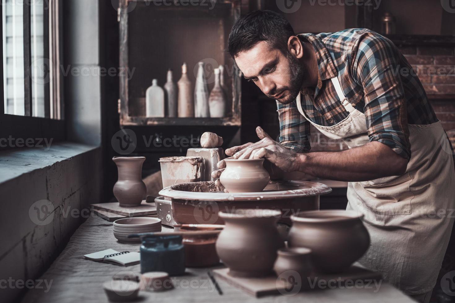 totale concentrazione a opera. fiducioso giovane uomo fabbricazione ceramica pentola su il ceramica ruota foto