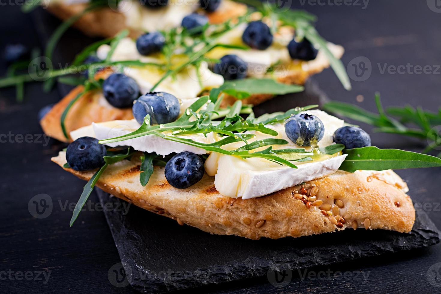 bruschetta. crostini crostini con fresco frutti di bosco mirtillo e Miele, Brie formaggio, rucola. italiano cucina foto