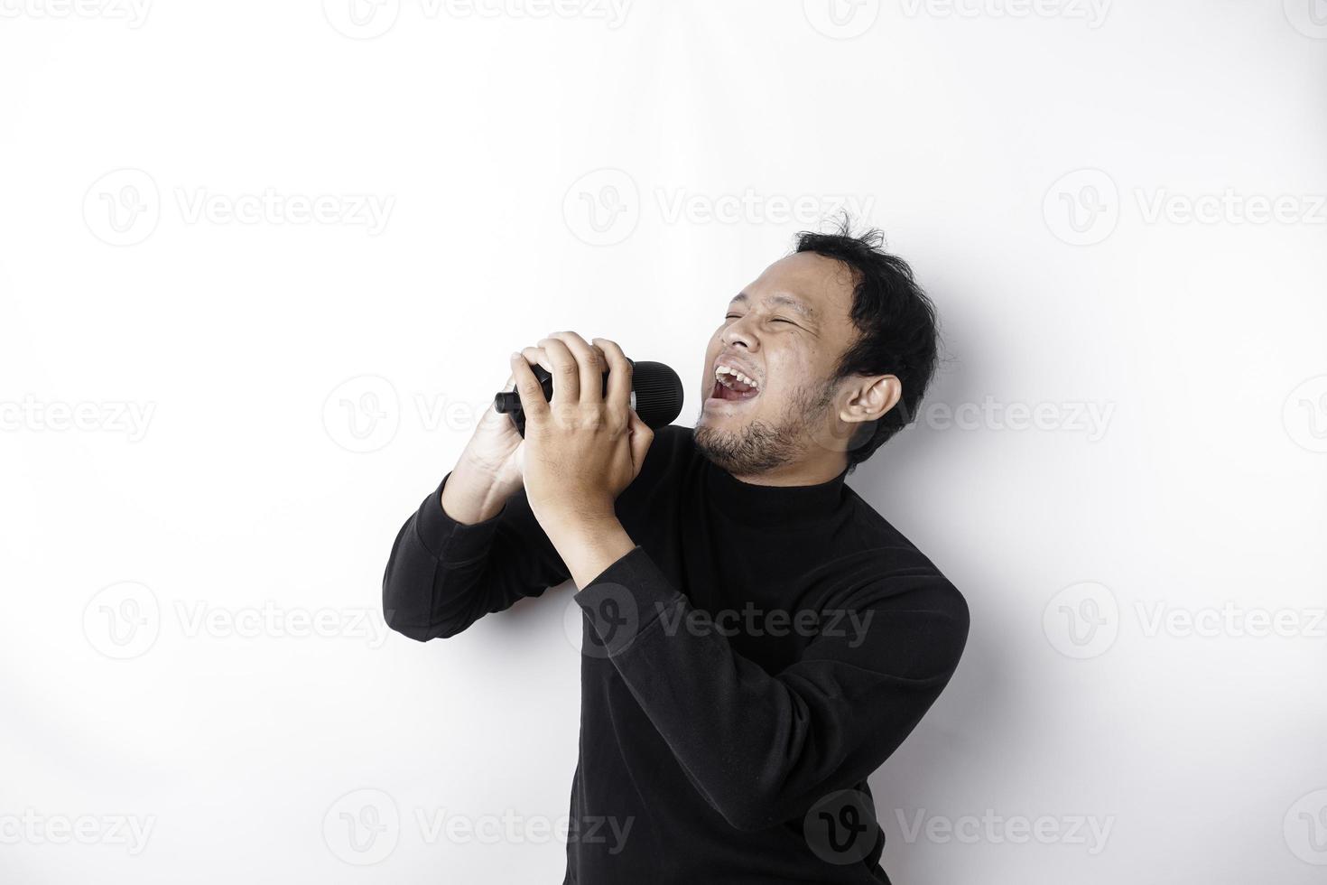 ritratto di spensierato asiatico uomo, avendo divertimento karaoke, cantando nel microfono mentre in piedi al di sopra di bianca sfondo foto