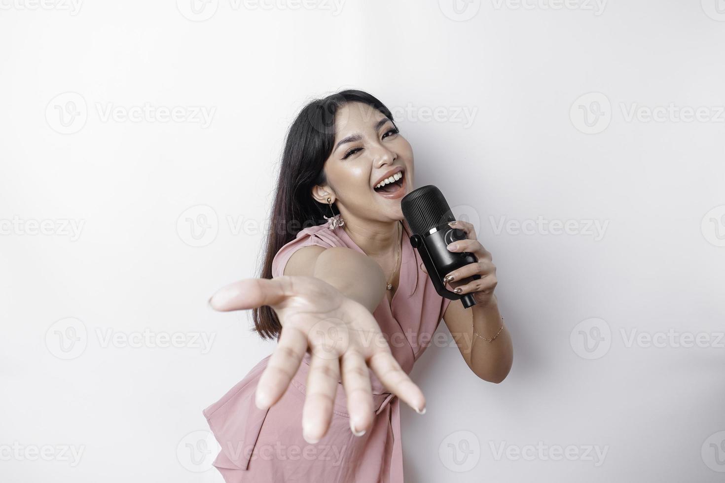 ritratto di spensierato asiatico donna, avendo divertimento karaoke, cantando nel microfono mentre in piedi al di sopra di bianca sfondo foto