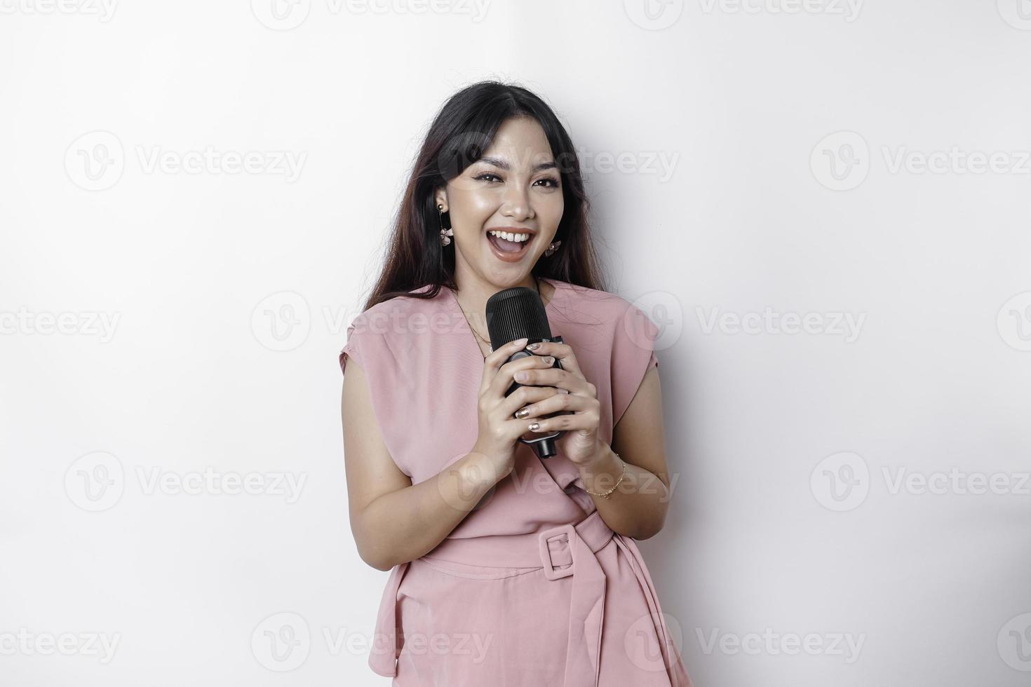 ritratto di spensierato asiatico donna, avendo divertimento karaoke, cantando nel microfono mentre in piedi al di sopra di bianca sfondo foto