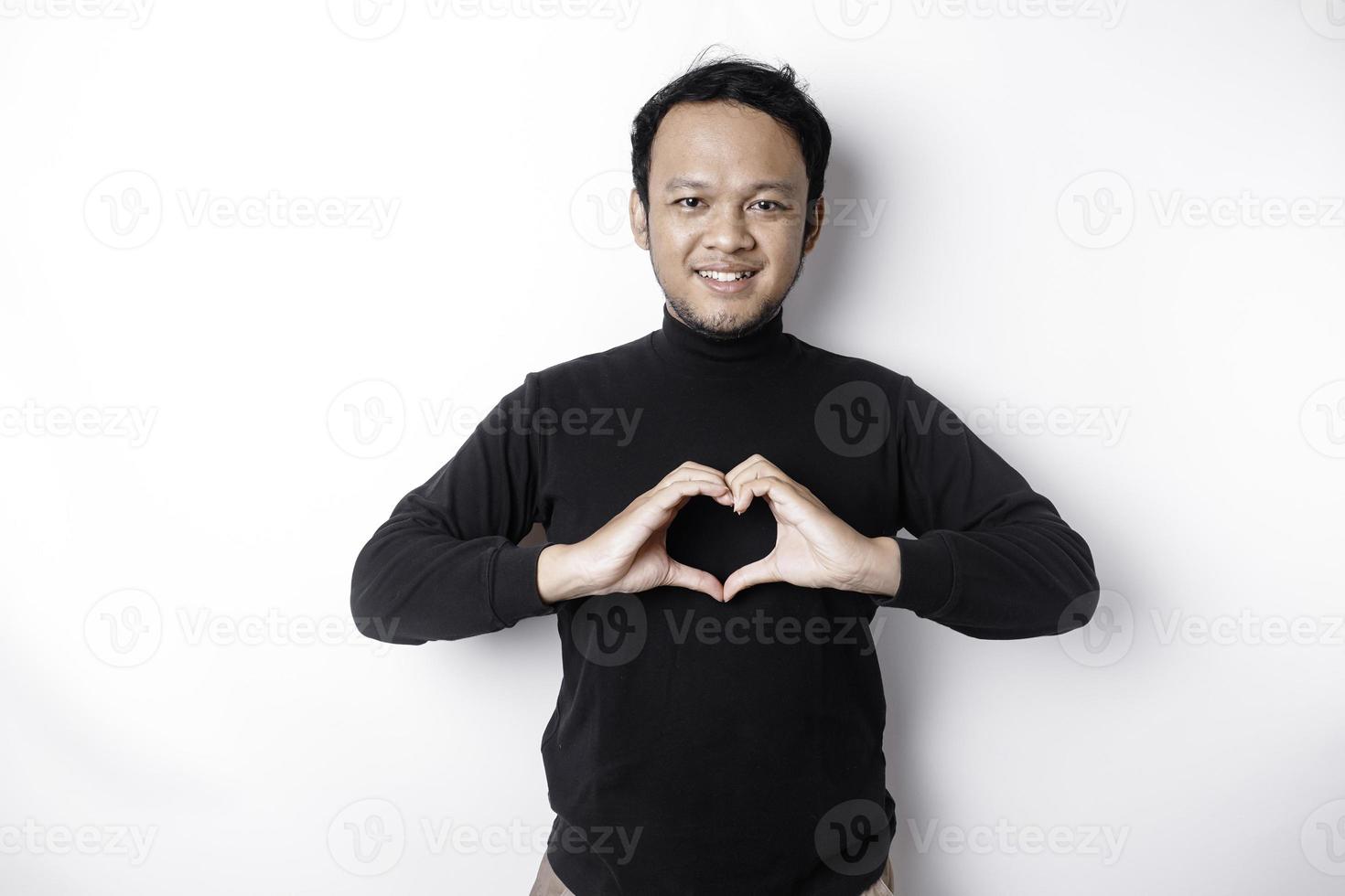 un' contento giovane asiatico uomo indossare un' nero camicia si sente romantico forme cuore gesto esprimendo tenero sentimenti foto