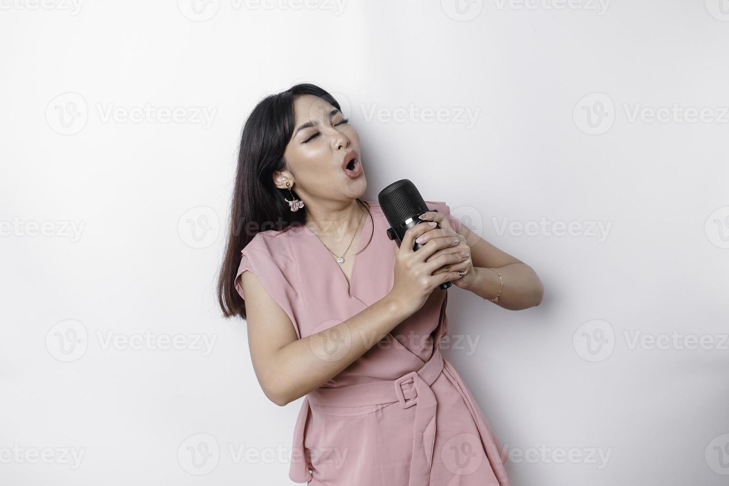 ritratto di spensierato asiatico donna, avendo divertimento karaoke, cantando nel microfono mentre in piedi al di sopra di bianca sfondo foto