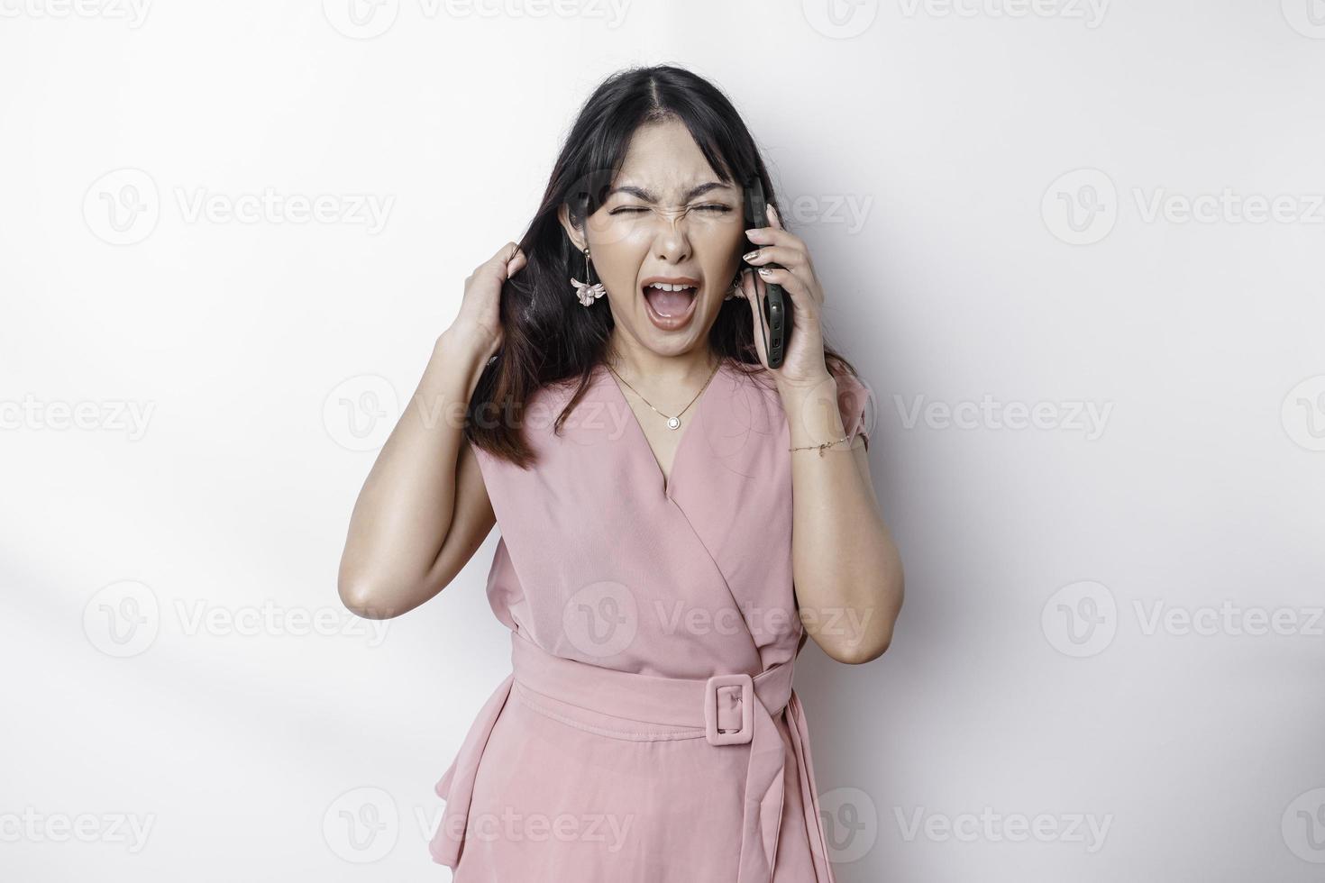 un' insoddisfatto giovane asiatico donna vestito nel rosa, sembra scontento con irritata viso espressioni Tenere sua Telefono foto