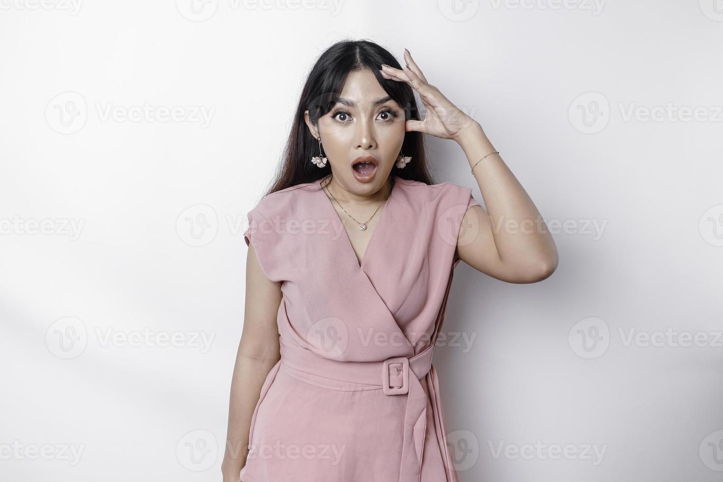 sorpreso giovane asiatico donna copertura bocca con mani e fissando a telecamera mentre in piedi contro bianca sfondo foto