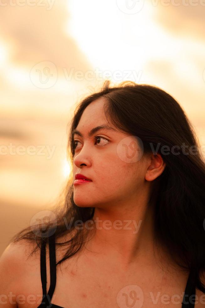 un asiatico donna con nero capelli e un' bellissimo viso in posa nel davanti di il spiaggia con caldo foto