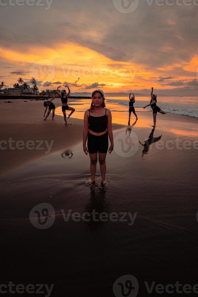 ritratto di un asiatico donna nel nero Abiti in piedi su il spiaggia con sua amici danza dietro a sua foto