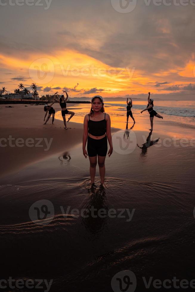 ritratto di un asiatico donna nel nero Abiti in piedi su il spiaggia con sua amici danza dietro a sua foto