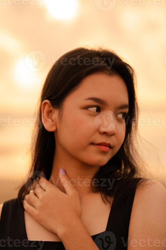 bellissimo asiatico donna con un' nero camicia e nero capelli sorridente con liscio pelle vicino il spiaggia foto