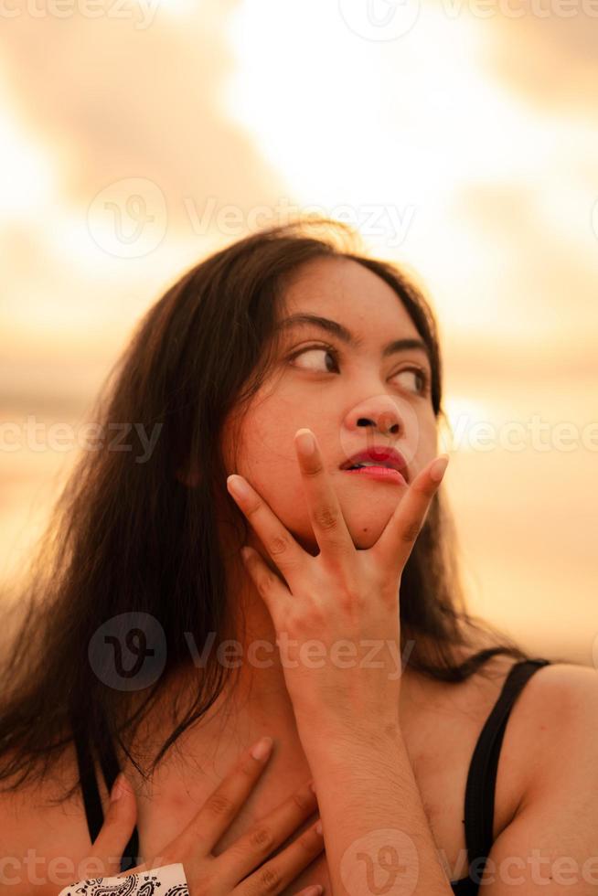 un asiatico donna con lungo nero capelli pose con sua mani mentre godendo il Visualizza di il spiaggia foto