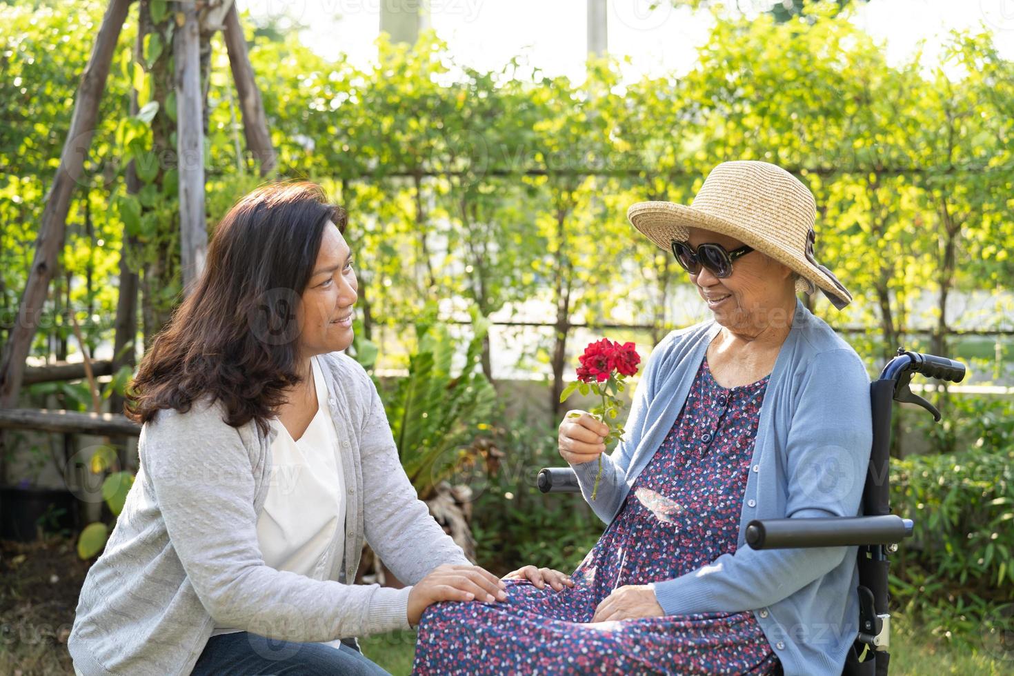 donna anziana asiatica o anziana che tiene fiore di rosa rossa, sorriso e felice nel giardino soleggiato. foto