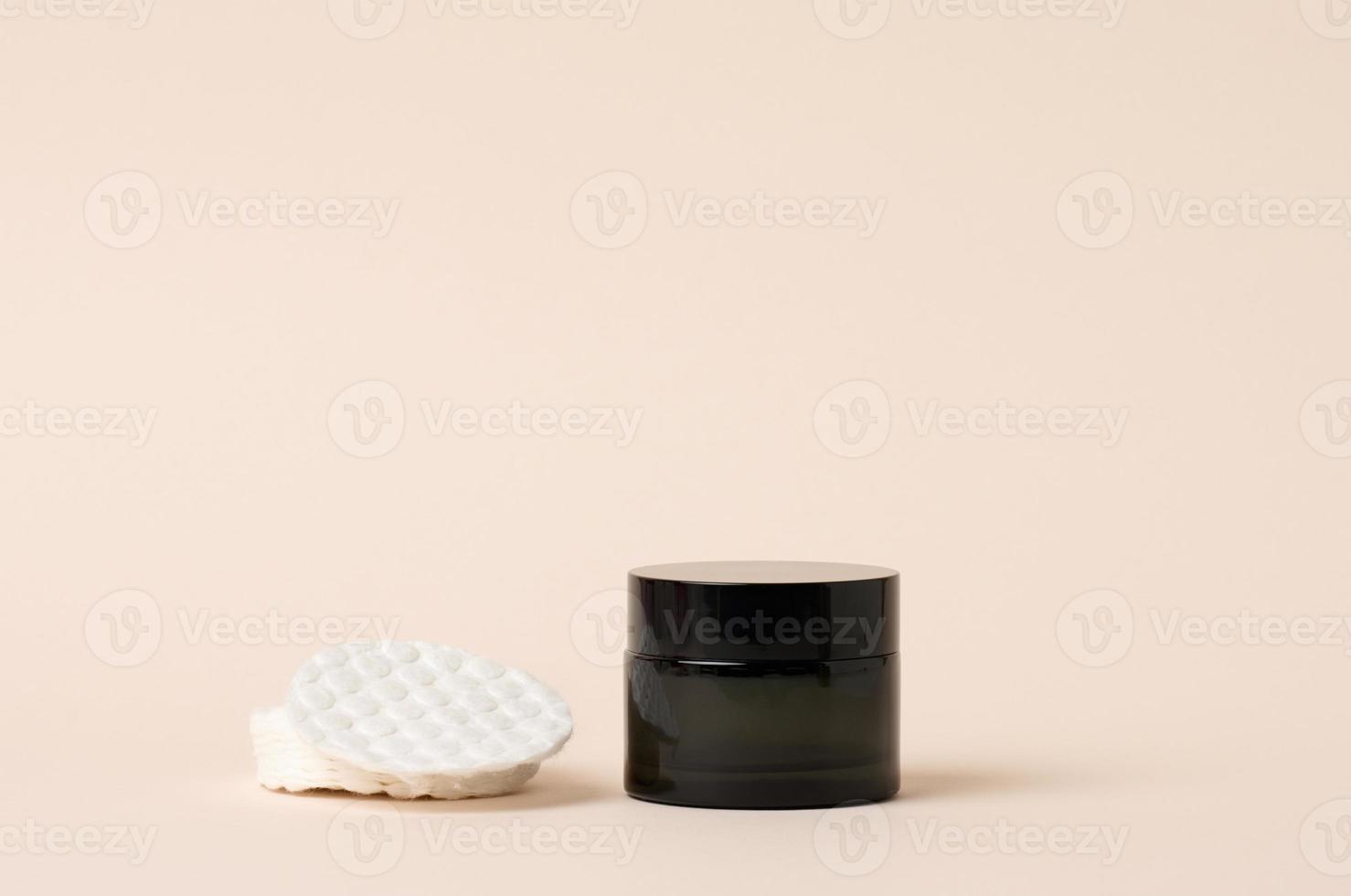 cosmetico prodotti nel un' nero bicchiere vaso con un' coperchio e bianca cotone pad. vuoto per il branding prodotti, idratante su beige sfondo foto