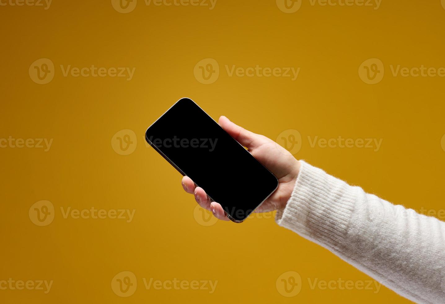 femmina mano Tenere smartphone con vuoto nero schermo su giallo sfondo foto