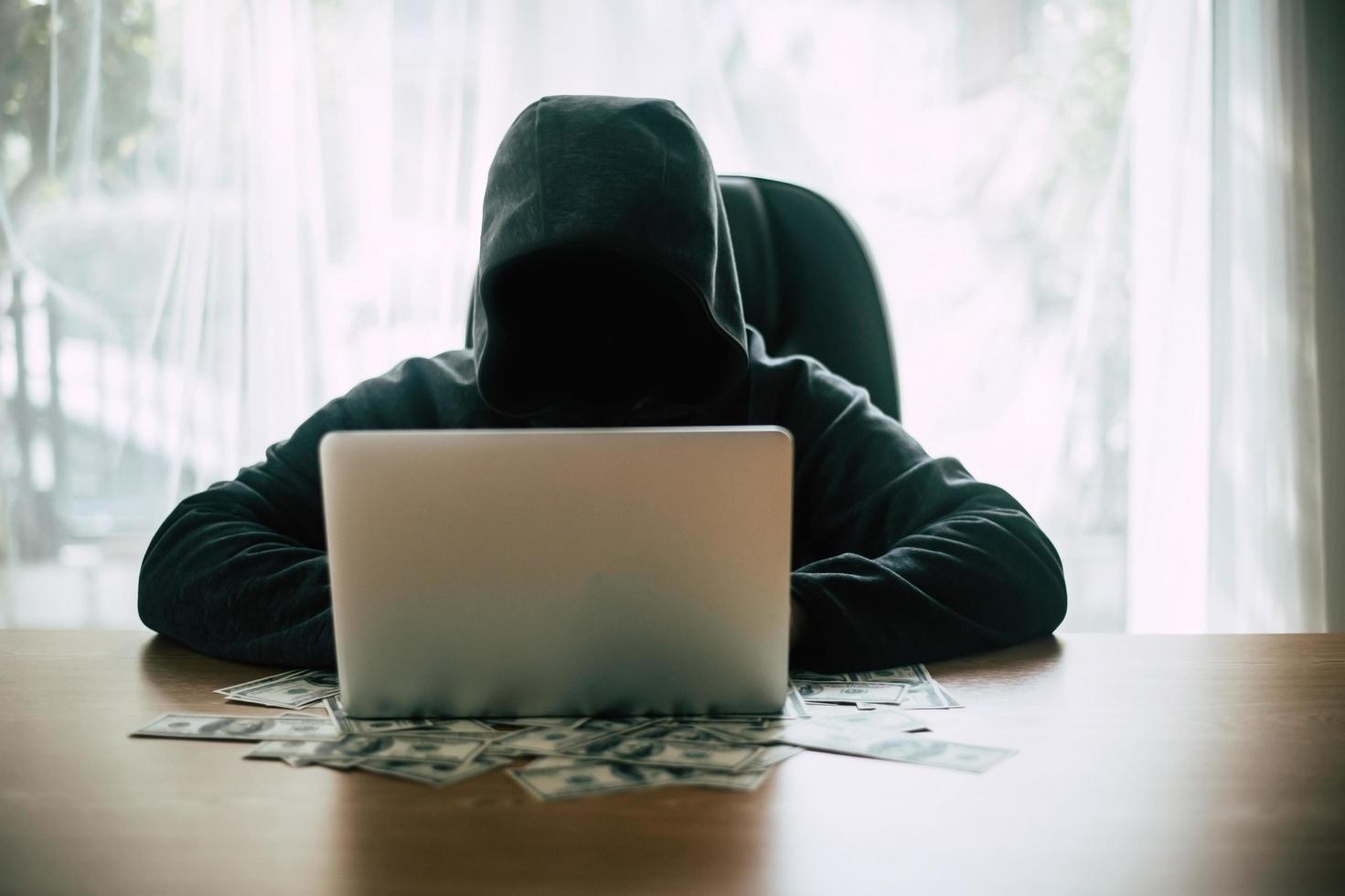 hacker davanti al suo computer con banconote in dollari foto