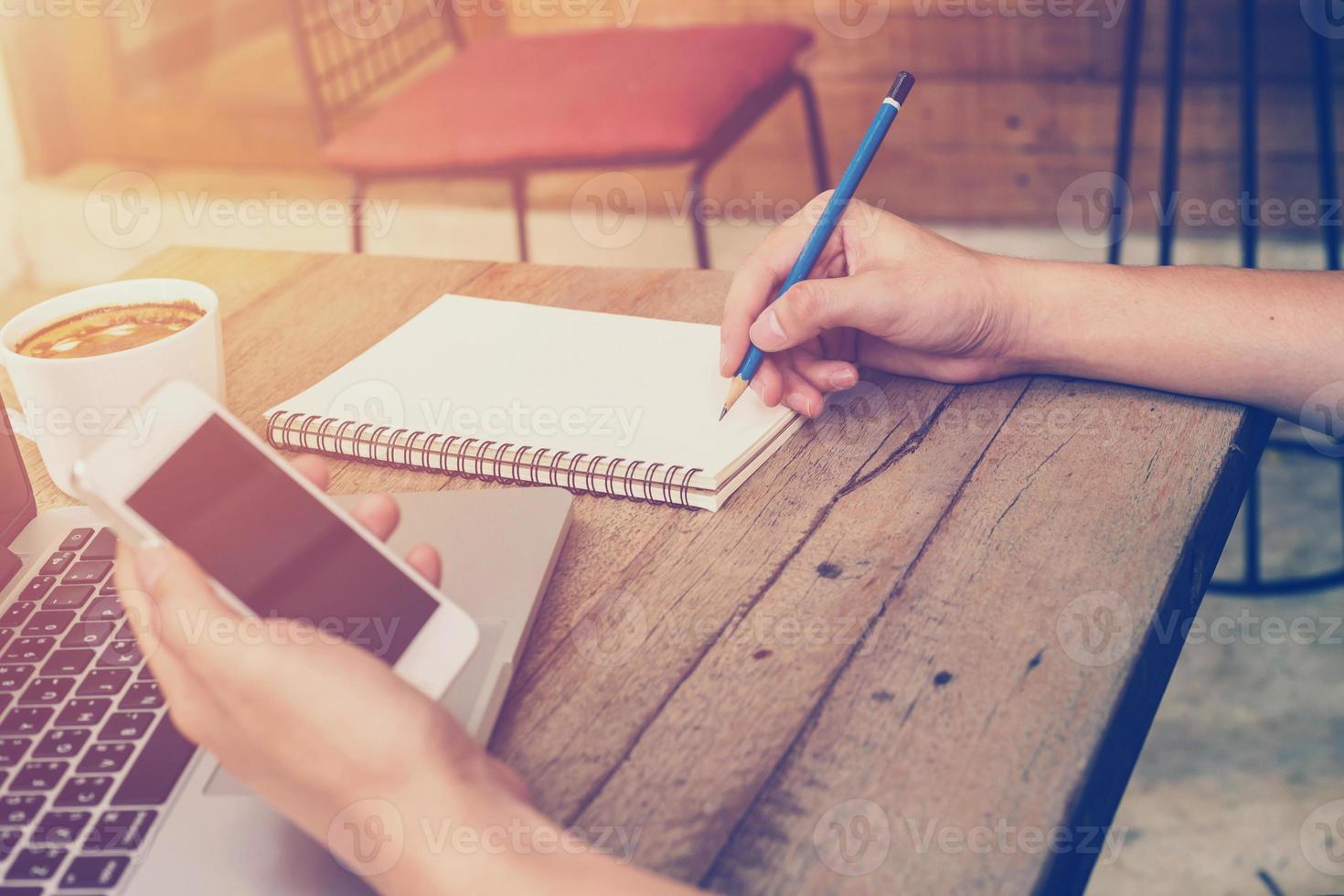 giovane attività commerciale uomo mano Tenere Telefono e scrittura e utilizzando il computer portatile nel caffè negozio con Vintage ▾ filtro. foto