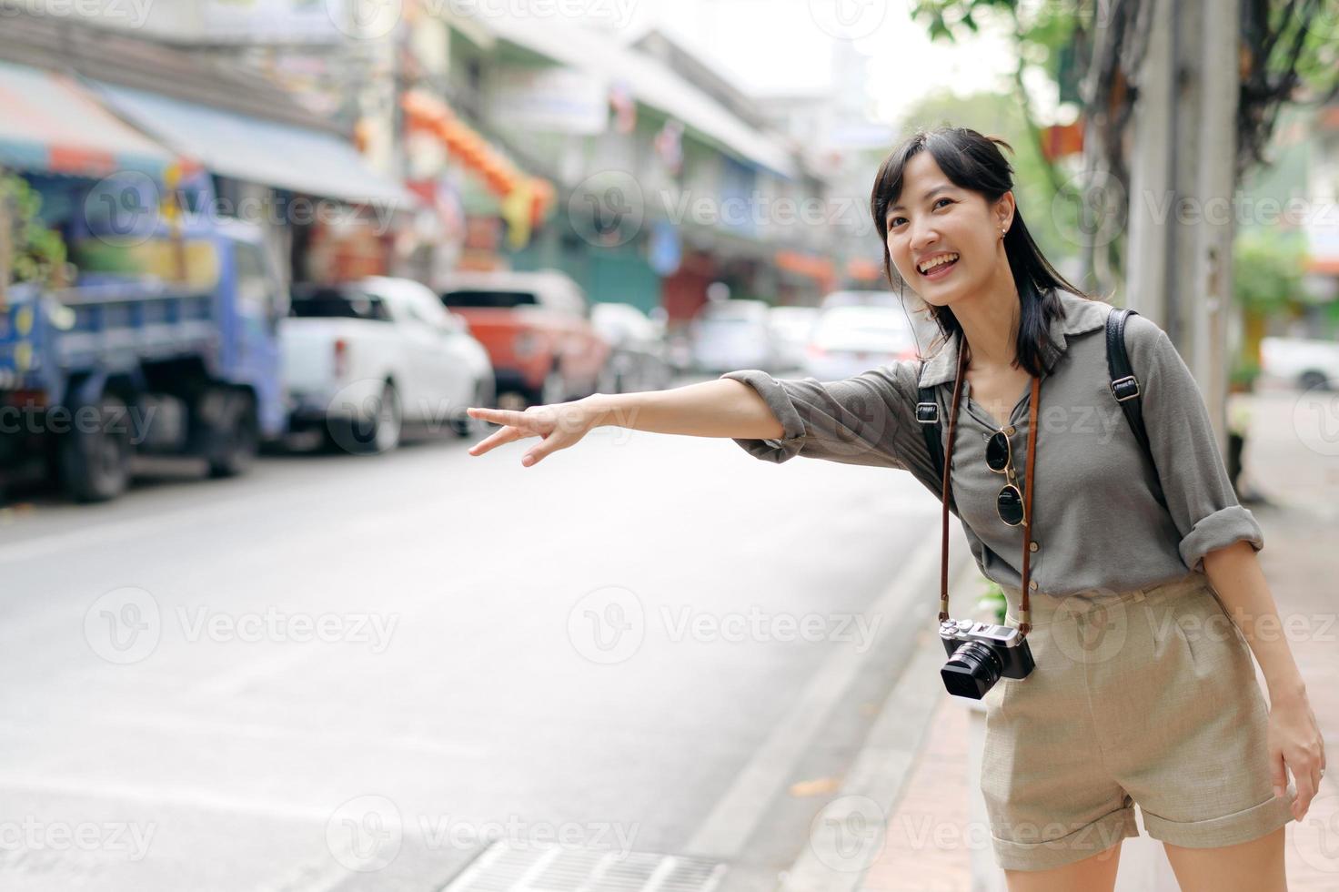 sorridente giovane asiatico donna viaggiatore autostop su un' strada nel il città. vita è un' viaggio concetto. foto