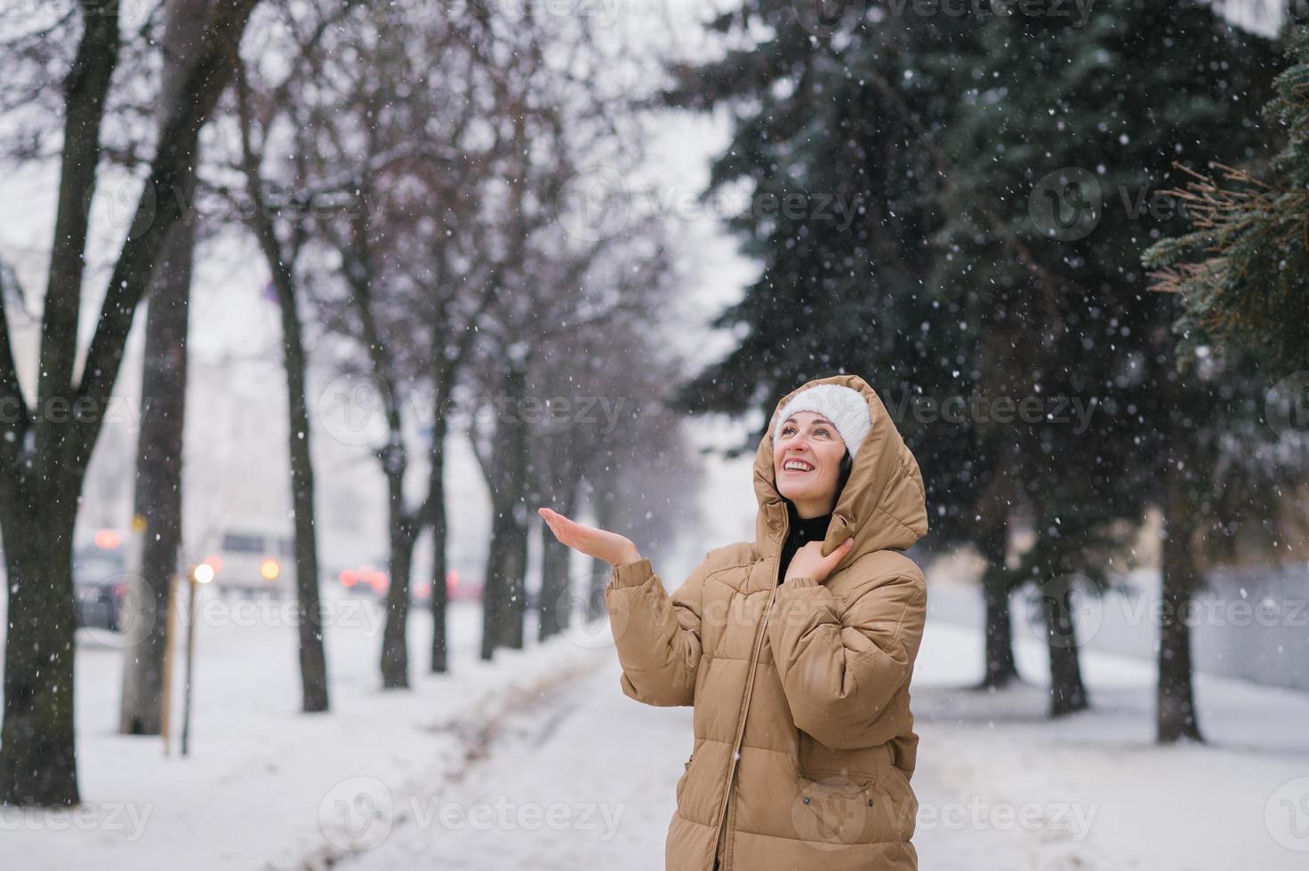 un' contento donna nel un' incappucciato cappotto. esso sta nel il città nel inverno sotto il neve foto