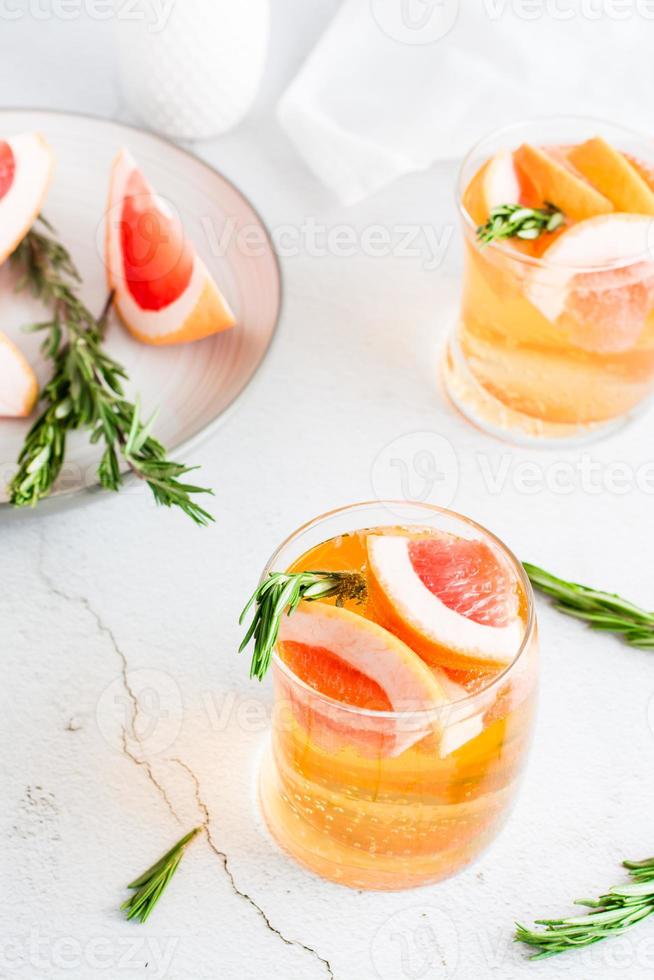 rinfrescante pompelmo cocktail con rosmarino nel bicchieri e frutta su un' piatto su il tavolo. fatti in casa bere. verticale Visualizza foto